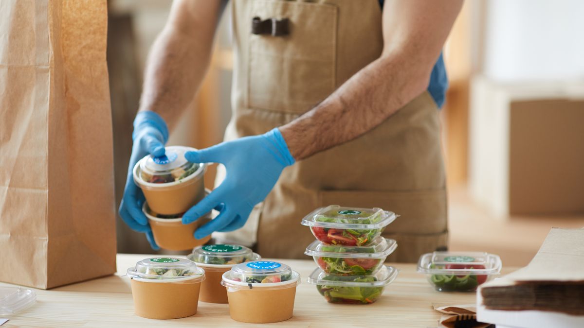 Closeup of a worker wearing protective gloves packaging food orders.