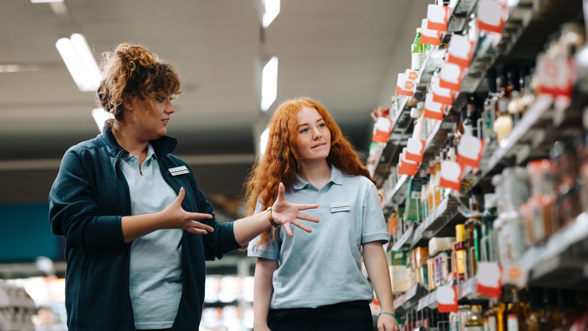 Grocery store worker showing items in an isle to another worker.